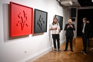 Łukasz Gawron Jan Sętowski i Robert Jasiak stojący przed wystawionymi pracami artystycznymi w galerii sztuki