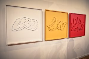 prace artystyczne przedstawiające przetworzony znak graficzny marki Lego, od lewej w kolorach: białym, żółtym, czerwonym