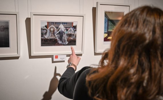 kobieta stojąca tyłem wskazująca palcem na fotografię zawieszoną na ścianie