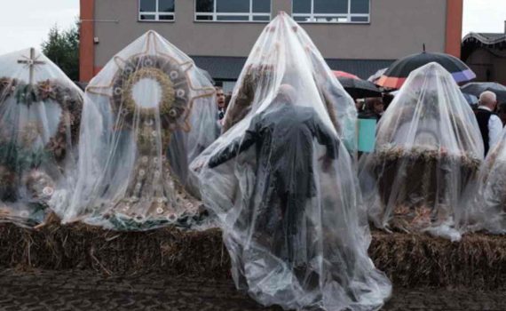 starszy mężczyzna kryjący się pod foliową plandeką, pod którymi znajdują się wieńce dożynkowe