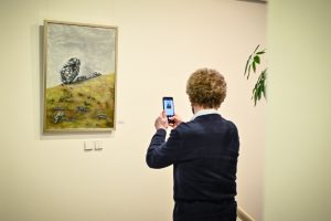 mężczyzna z telefonem w ręku wykonujący fotografię obrazu powieszonego na ścianie