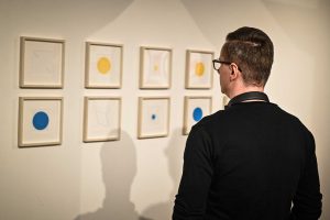 mężczyzna w okularach przyglądający się pracom plastycznym prezentowanym w galerii sztuki