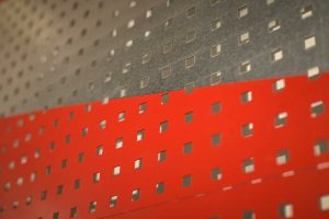 detal przedstawiający fragment pracy plastycznej Anny Szumigaj-Badziak powierzchnia perforowana kwadratowymi otworami, górna połowa w kolorze szarnym dolna połowa w kolorze czerwonym