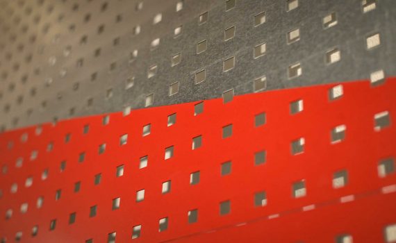 detal przedstawiający fragment pracy plastycznej Anny Szumigaj-Badziak powierzchnia perforowana kwadratowymi otworami, górna połowa w kolorze szarnym dolna połowa w kolorze czerwonym