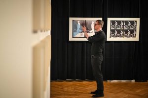 mężczyzna wykonujący fotografię obrazów w galerii sztuki ustawiony bokiem na tle dwóch innych obrazów