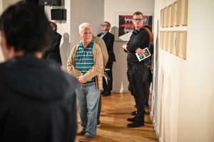 mężczyźni patrzący na rząd obrazów zawieszonych w galerii sztuki