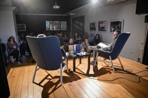 gość i prowadzący siedzący w fotelach na scenie przed publicznością