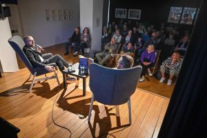 gość i prowadzący podczas spotkania autorskiego siedzący na scenie przed publicznością