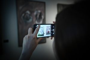 osoba wykonująca smartfonem fotografię obrazom podczas wystawy w galerii sztuki