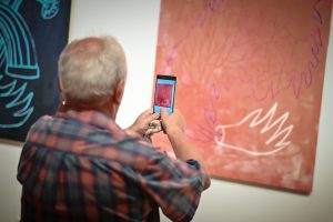 mężczyzna wykonujący smartfonem zdjęcie obrazu w galerii sztuki