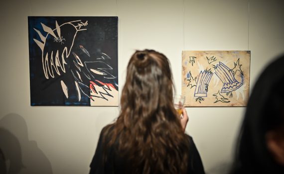 kobieta stojąca tyłem oglądająca obrazy podczas wernisażu wystawy