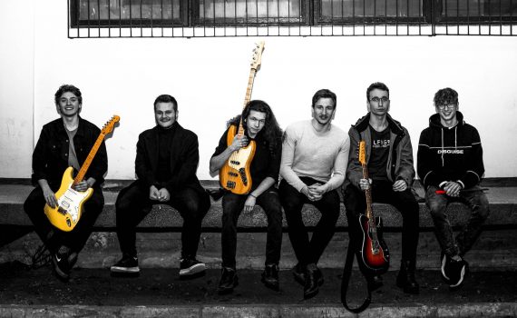 muzycy zespołu Fuzz'Ya siedzący na murku z instrumentami w dłoniach