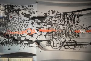 mural Bartłomieja Stypki przedstawiający kolaż różnych figur i znaków, zawierający zdeformowaną głowę oraz napis w języku angielskim z wyrazem UNCONTROLLABLE