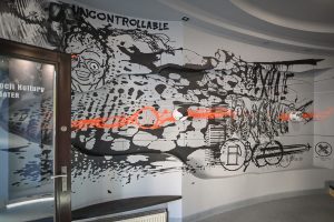 fragment drzwi wejściowych do Ośrodka Promocji Kultury Gaude Mater zawierajace niepełny napis z nazwą instytucji oraz fragment muralu Bartłomieja Stypki