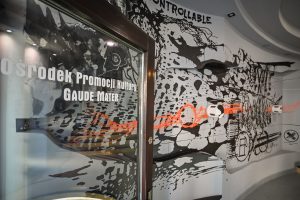 drzwi wejściowe do Ośrodka Promocji Kultury Gaude Mater zawierajace napis z nazwą instytucji oraz fragment muralu Bartłomieja Stypki