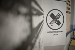 sygnatura Bartłomieja Stypki w formie znaku X wpisanego w okrąg z napisem zawierającym jego imię i nazwisko oraz poniżej liczba zawierająca aktualny rok 2022