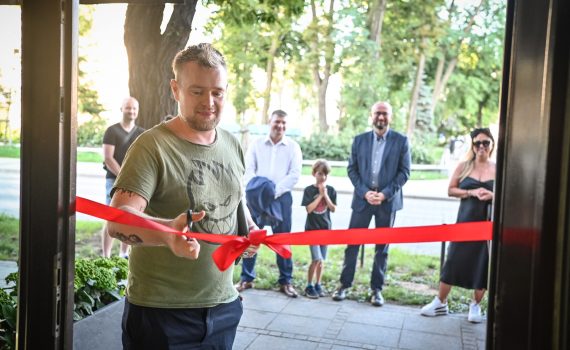 Bartłomiej Stypka przecinający czerwoną wstęgę podczas odsłonięcia swojego muralu w Ośrodku Promocji Kultury Gaude Mater w Częstochowie