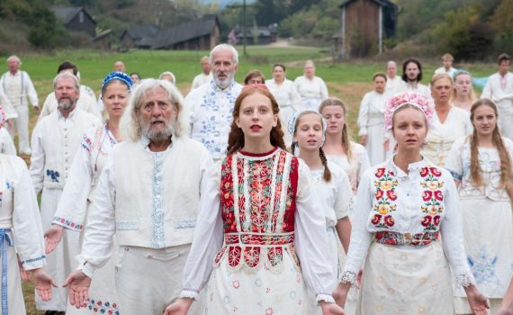 kadr z filmu w reżyserii Ariego Astera zatytułowanego Midsommar grupa osób ubranych w białe ludowe stroje rozkładający ramiona z uchylonymi ustami