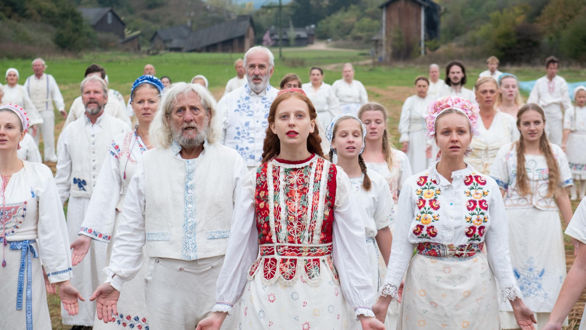 kadr z filmu w reżyserii Ariego Astera zatytułowanego Midsommar grupa osób ubranych w białe ludowe stroje rozkładający ramiona z uchylonymi ustami