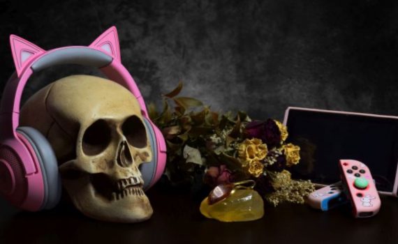 obraz z wystawy modern vanitas przedstawiający trupią czaszkę w różowych słuchawkach z kocimi uszami po lewej, wysuszone kwiaty pośrodku oraz konsolę do gry po prawej