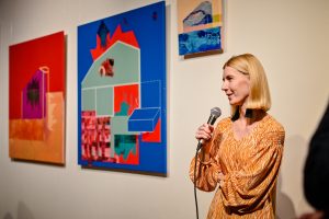 Justyna Warwas stojąca na tle swoich obrazów w galerii sztuki