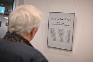 mężczyzna czytający informację biograficzną na temat Marii Cieślak-Gurgul zawieszoną na ścianie galerii sztuki